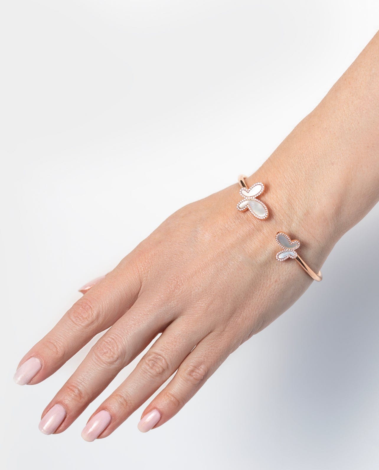 Hand wearing two butterfly-shaped rings on a light gray background