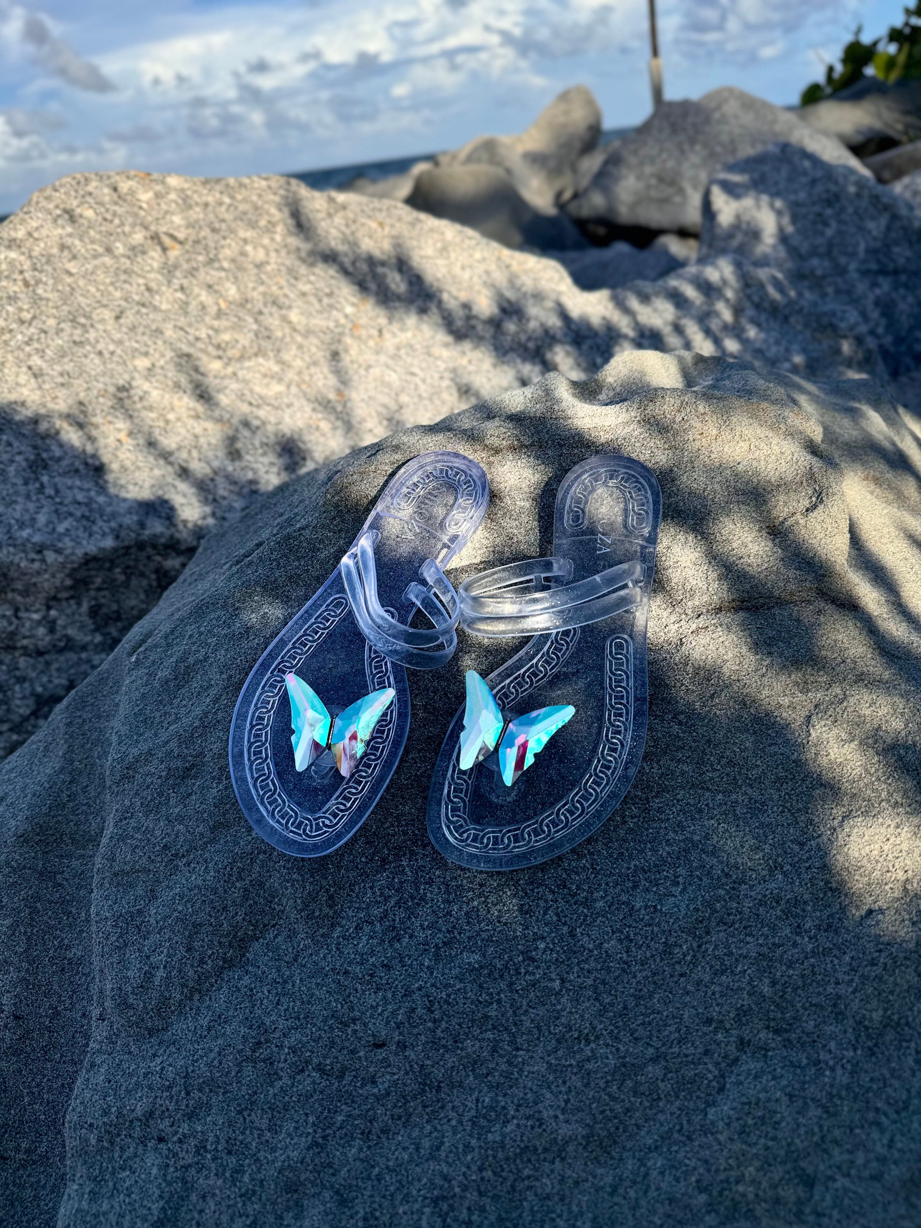 Clear sandals with butterfly designs on a rock by the ocean