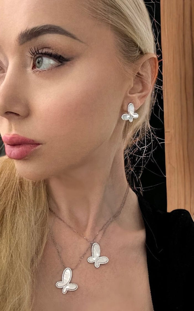 Woman wearing butterfly-shaped earrings and a necklace with a neutral background