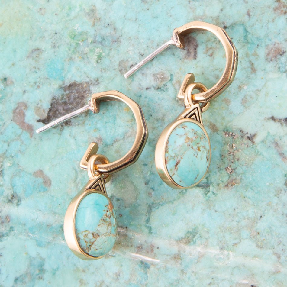 Gold earrings with turquoise stones on a textured turquoise background