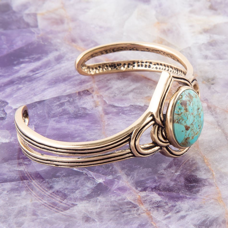 Gold bracelet with a turquoise stone on a purple marble background
