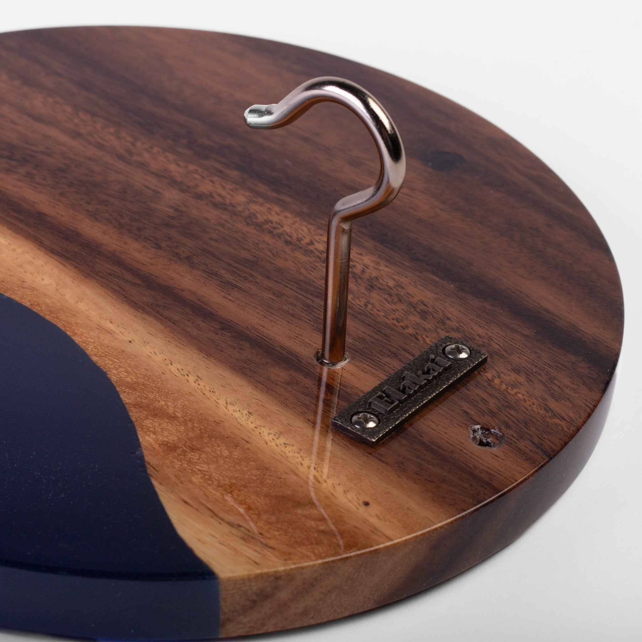 Close-up of a round wooden wall hook with a polished metal S-shaped hook mounted on a dark wood panel with a blue inlay.