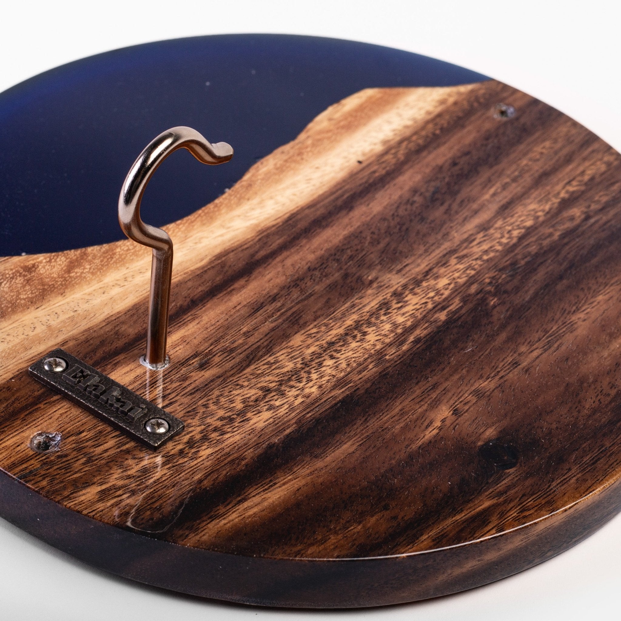 Close-up of a round wooden board with a dark blue resin inlay, a metal hook, and a small branded tag that reads 'SILKSTITCH'.