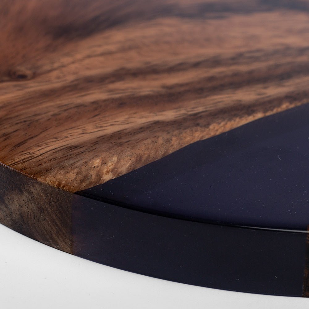 Close-up of a round wooden tray or board with a rich brown wood grain and a glossy black resin inlay, shown on a white surface.