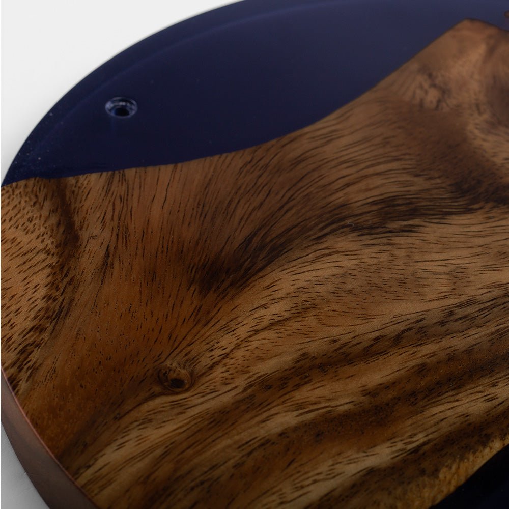 Close-up of a guitar body featuring a rich wavy wood grain pattern in warm brown tones, accented by a dark navy blue upper section.