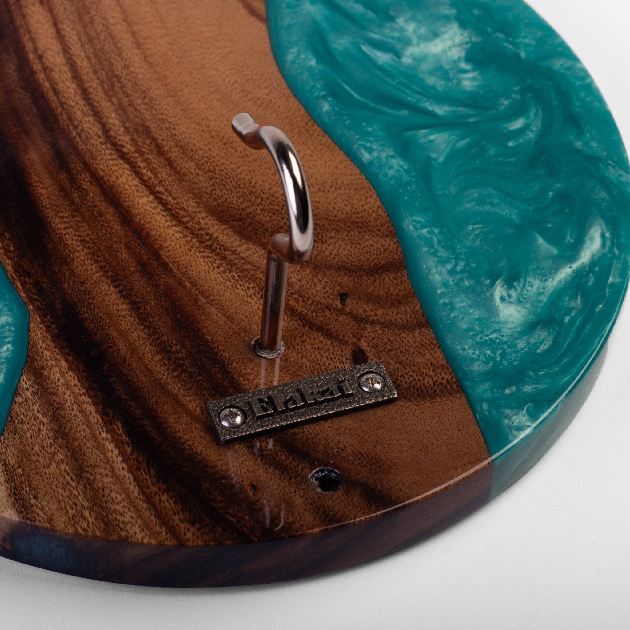 Close-up of a round wooden coat rack with a natural brown wood grain and a turquoise resin inlay, featuring a silver metal hook and a small metal brand plate reading 'HARPER'.