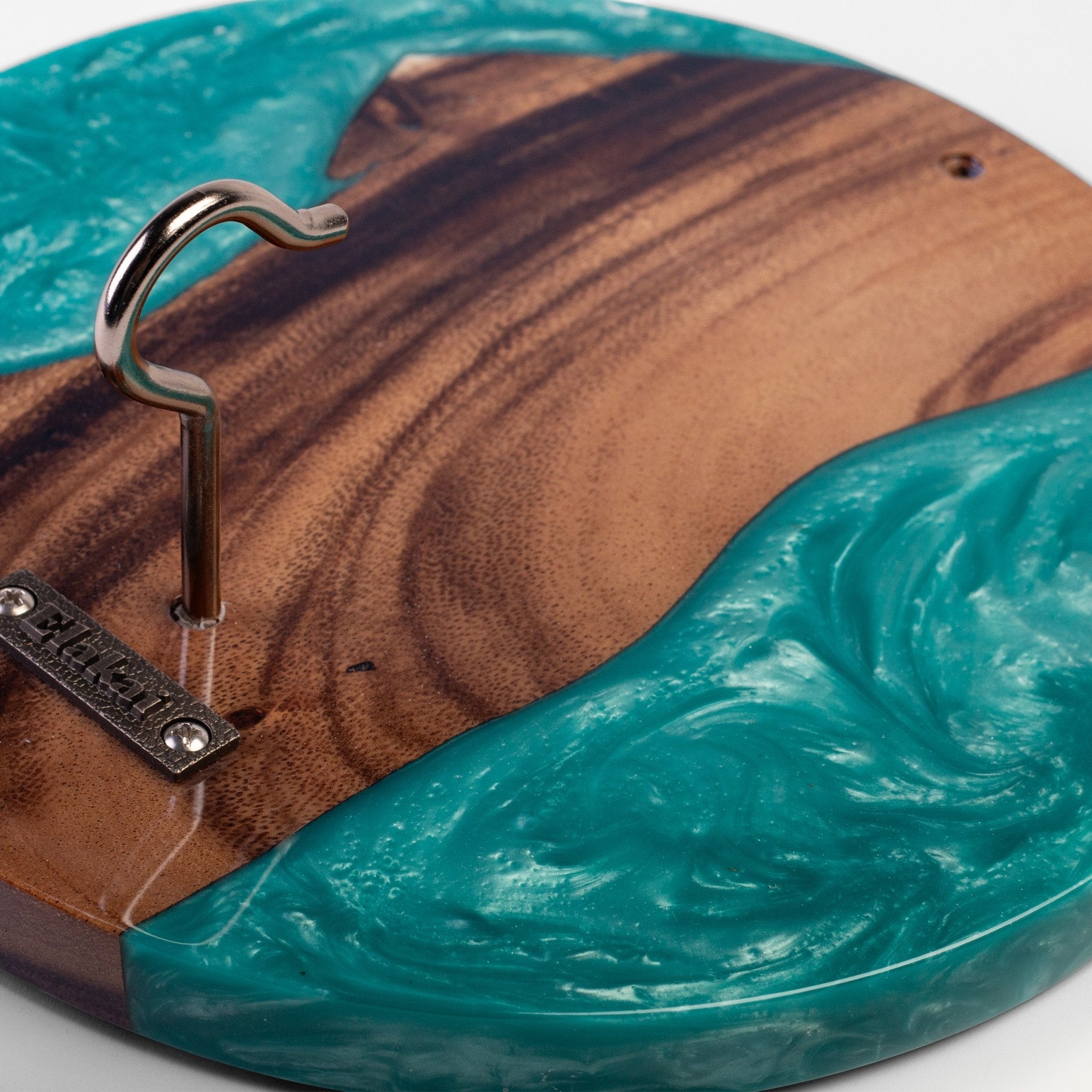 Close-up of a round wooden board or tray with a hanger hook mounted on the side. The wood has a rich brown grain, with a glossy teal resin inlay flowing around the edge.