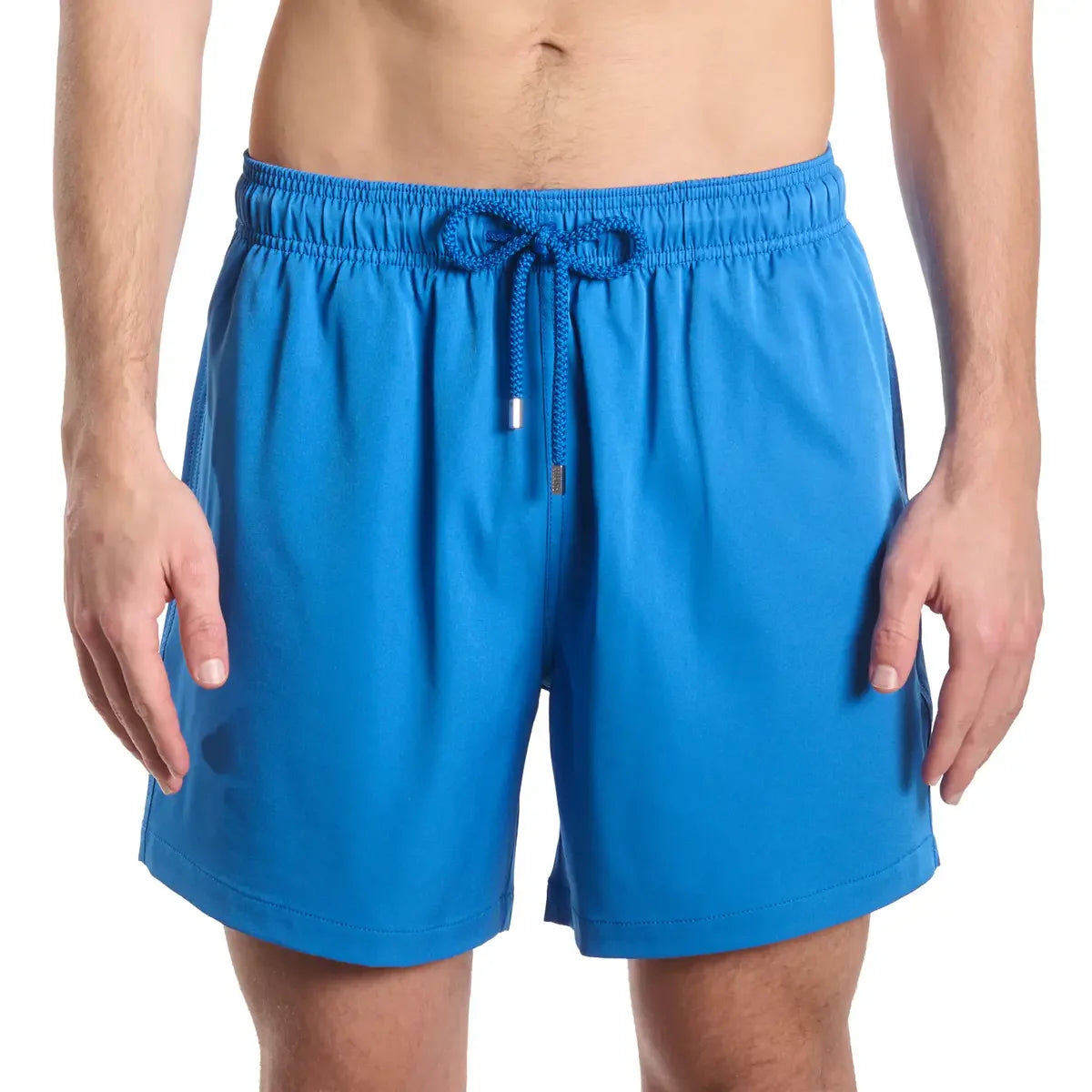 Blue swim shorts worn by a person on a white background