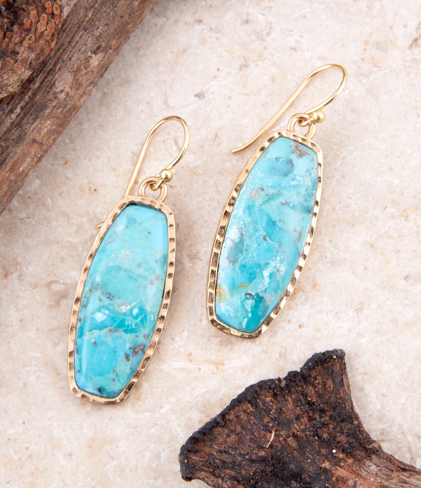 Turquoise earrings with gold frames on a textured surface