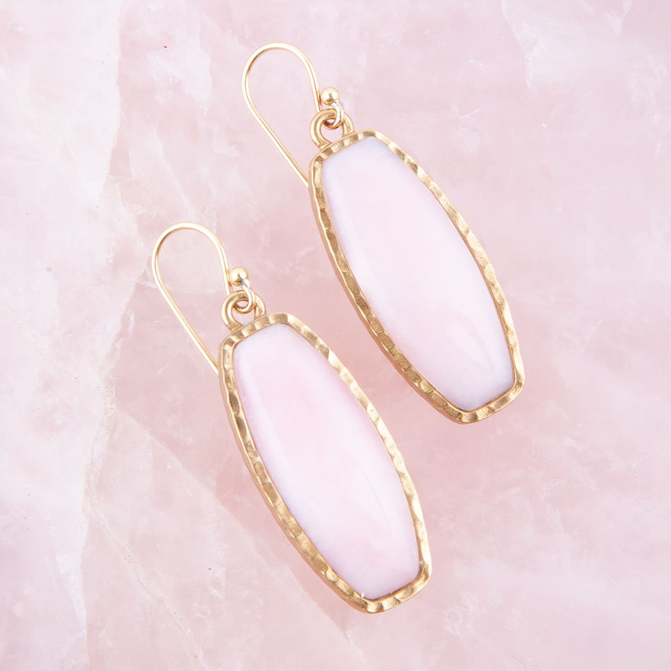 Gold-framed white earrings on a pink stone background