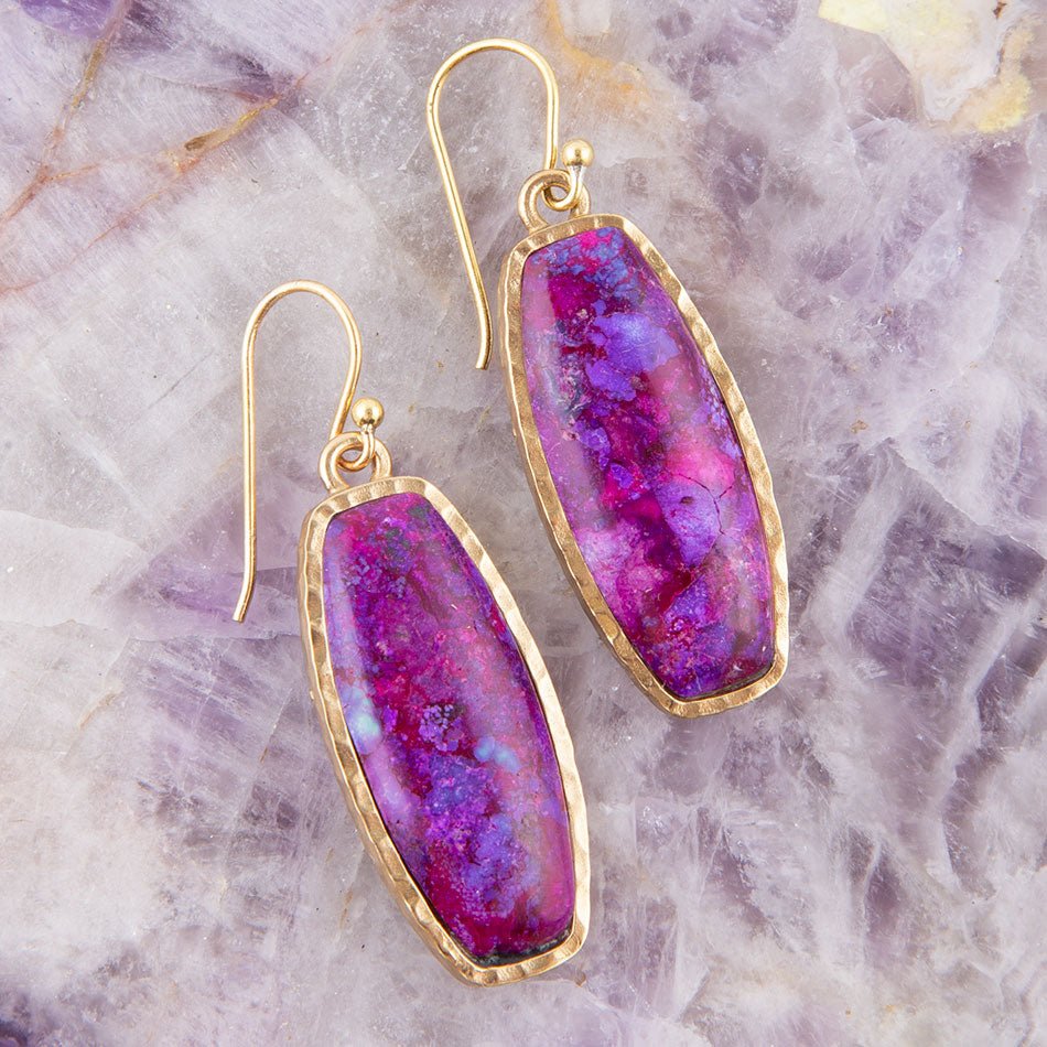 Purple stone earrings with gold frames on a textured purple surface