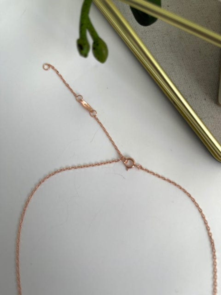 Rose gold necklace on a white surface with a plant in the background
