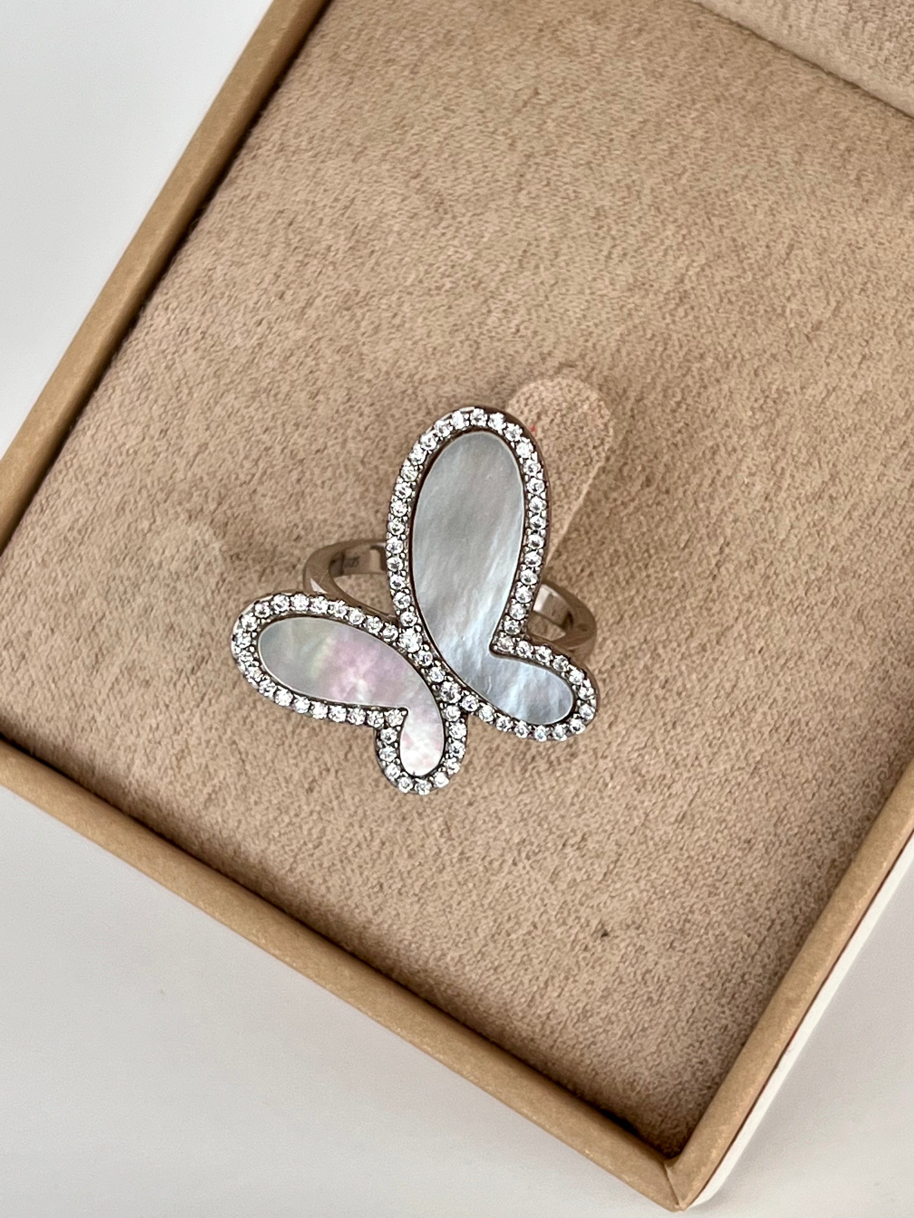 Butterfly-shaped ring with gemstones on a beige cushion in a box