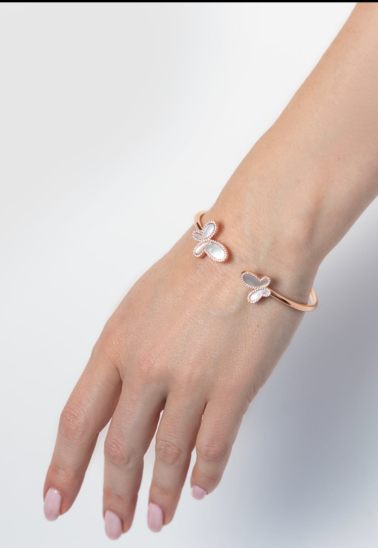 Rose gold bracelet with butterfly charms on a hand against a light gray background