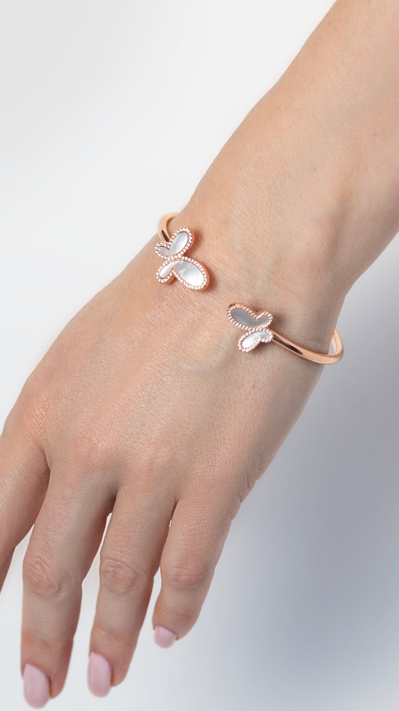 Hand wearing a rose gold butterfly bracelet on a light gray background