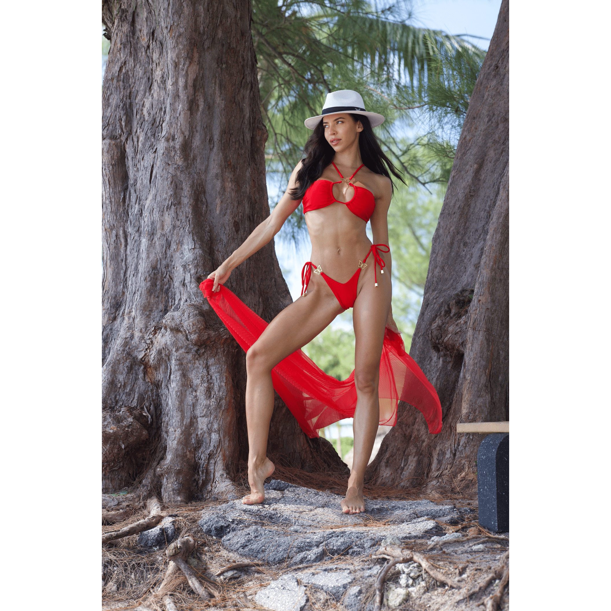 Woman in a red bikini and hat standing by a large tree