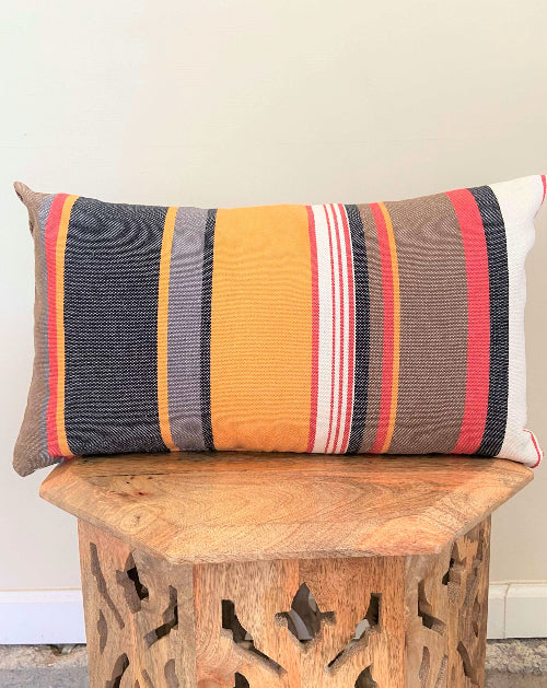 Striped pillow on a wooden stool against a neutral wall