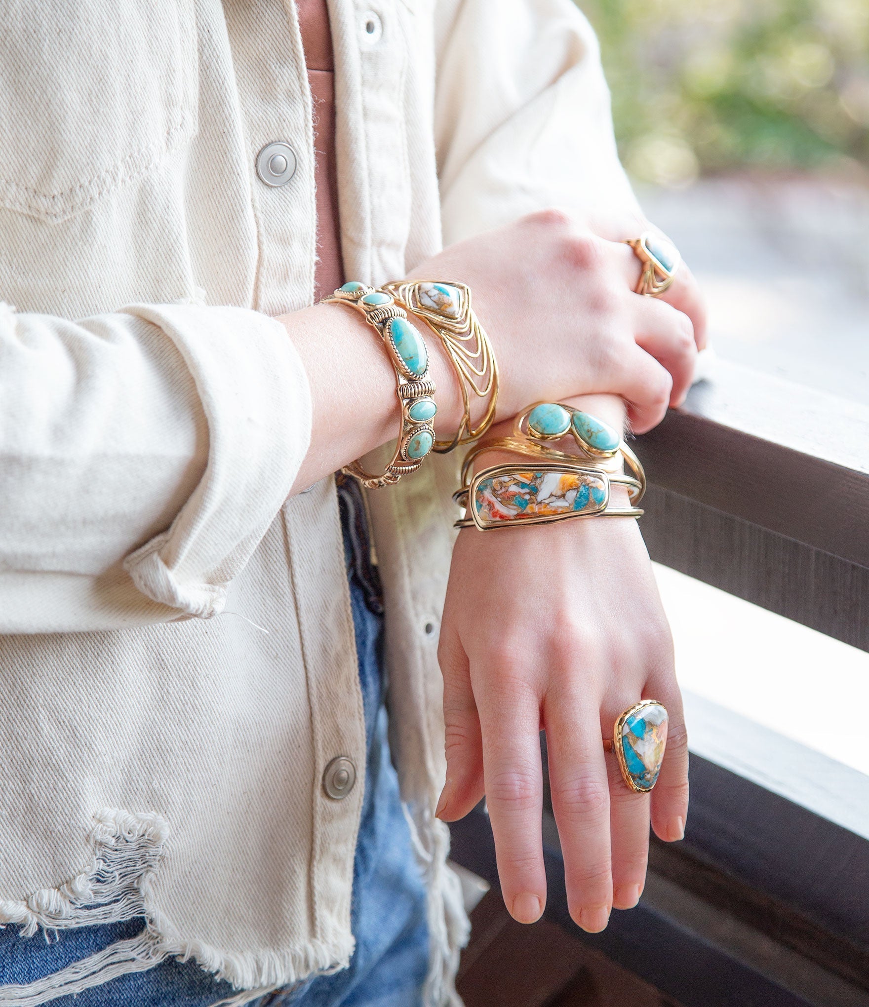 Close-up of hands wearing gold and turquoise jewelry with a blurred background