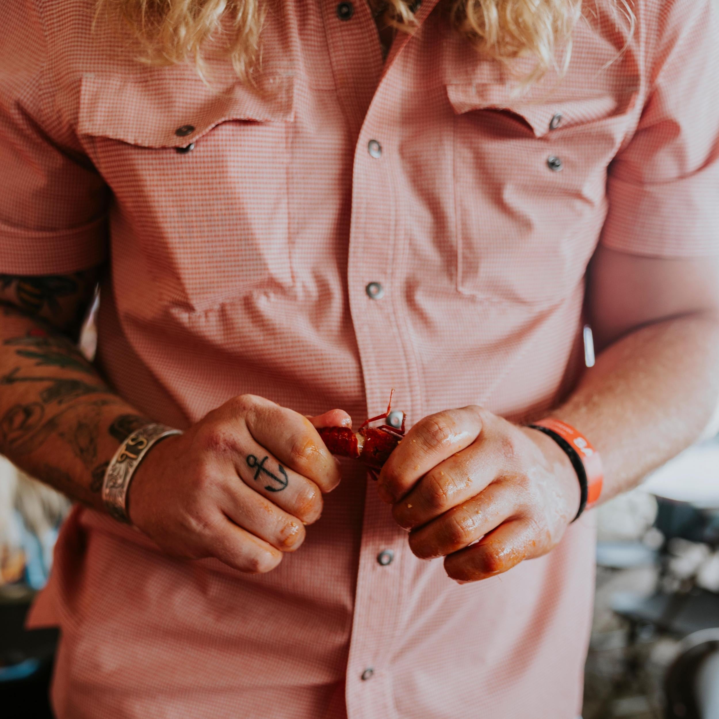 Person wearing a pink shirt with tattoos on arms holding a small object.