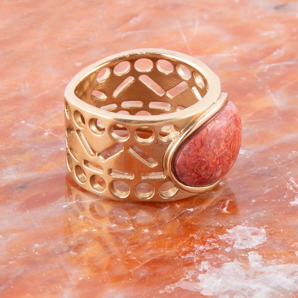 Gold ring with a red stone on a textured orange surface