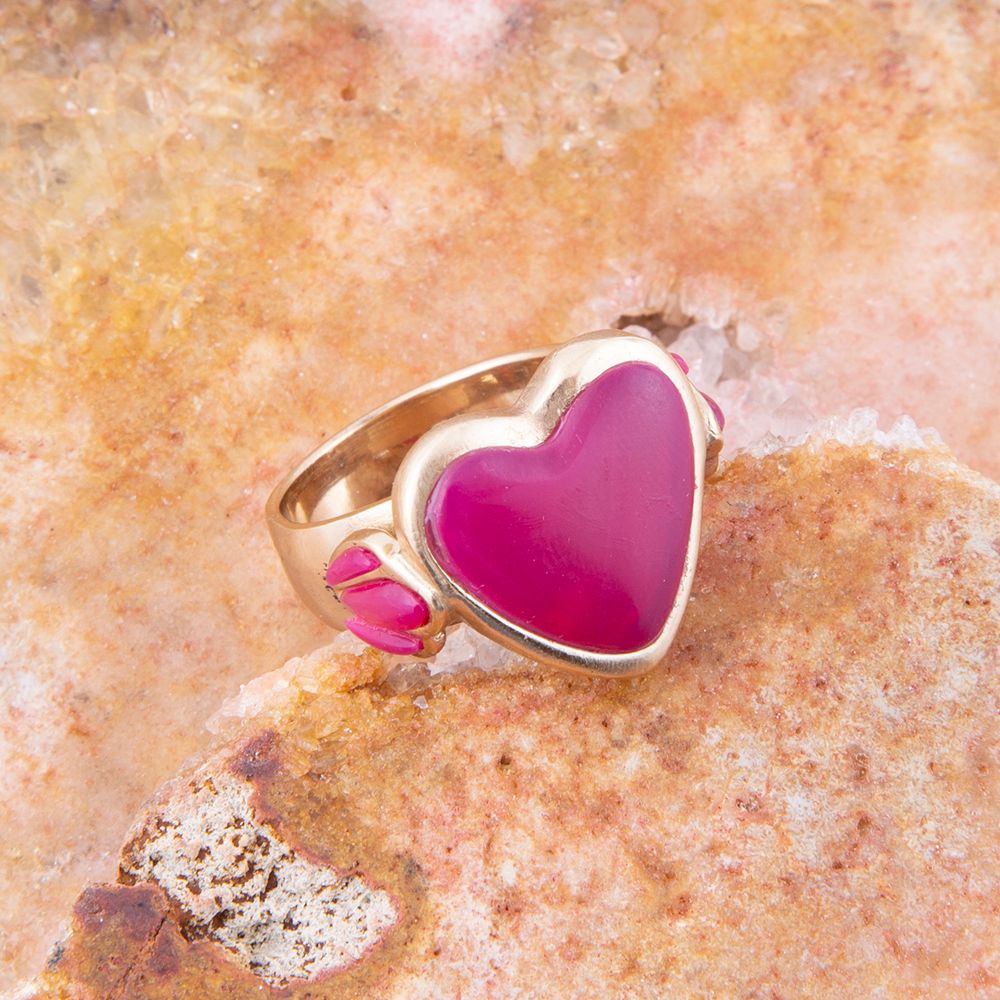 Gold ring with a pink heart-shaped stone on a textured beige surface