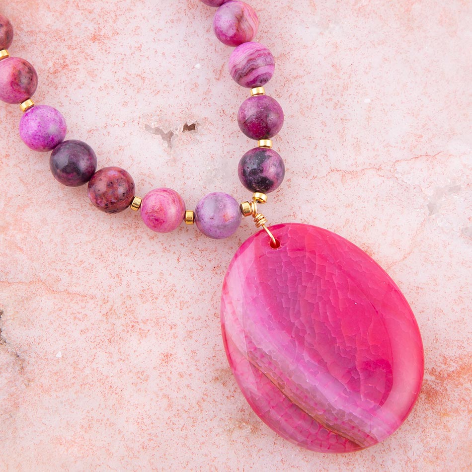 Necklace with pink and purple beads and a large pink pendant on a light pink background