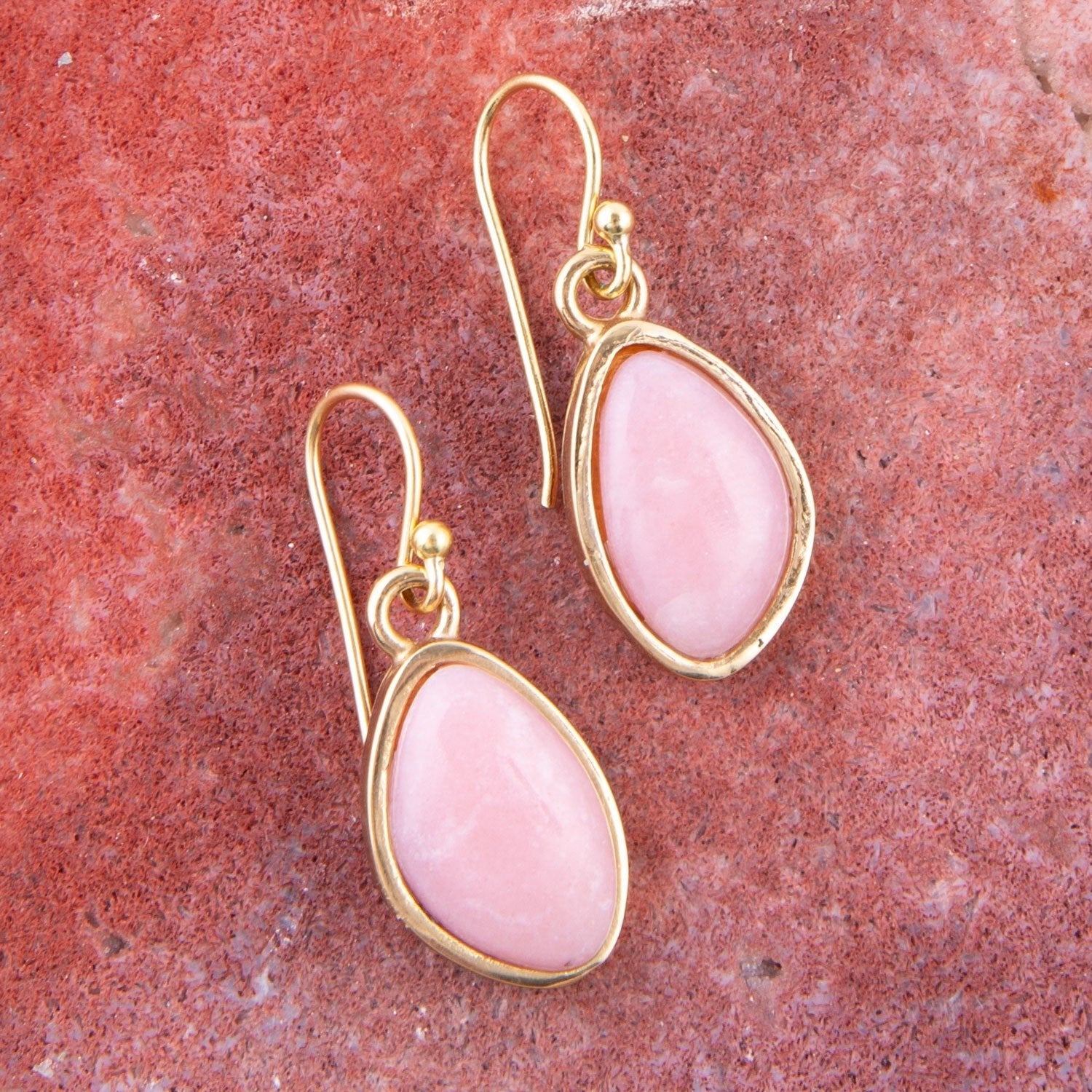 Gold earrings with pink stones on a red stone background
