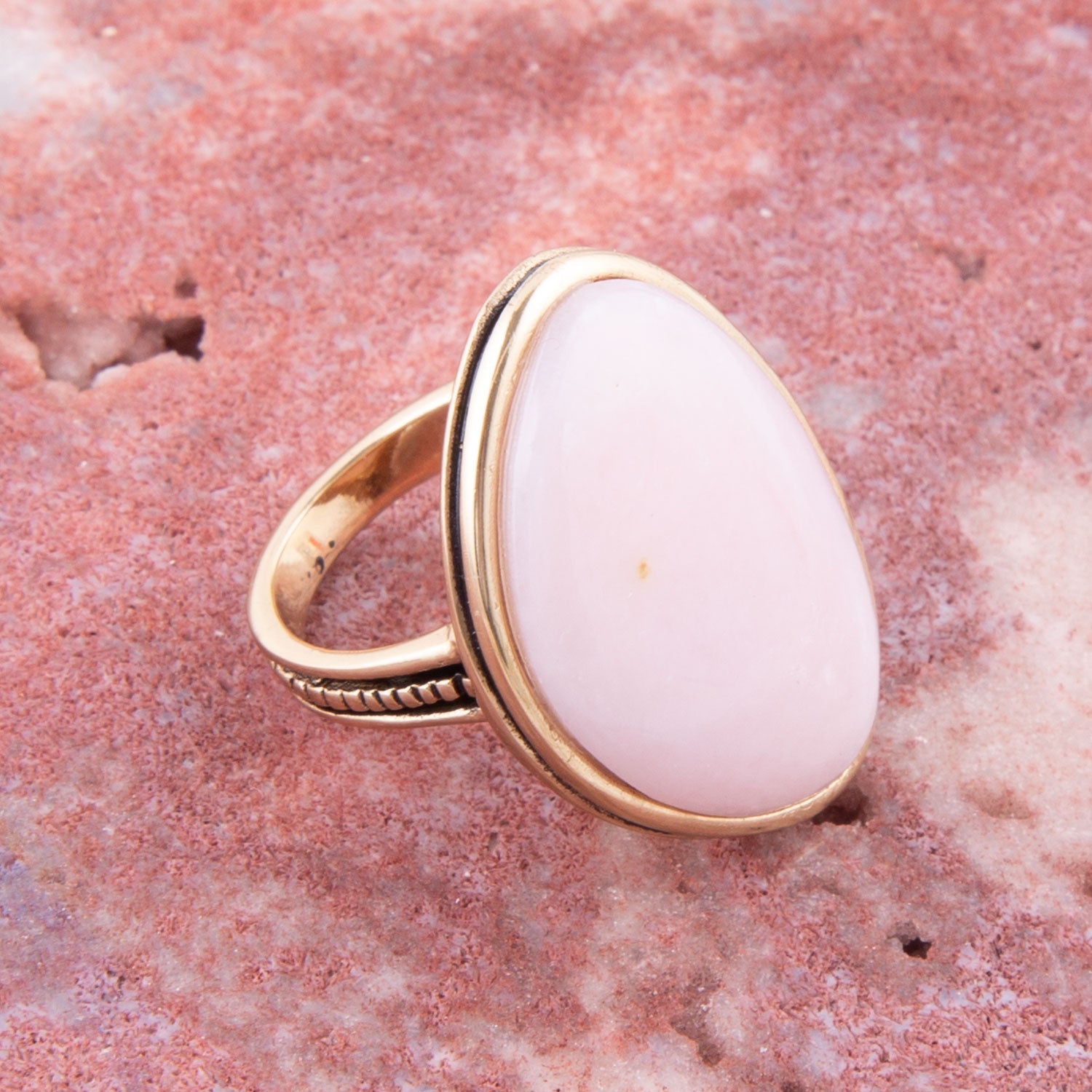 Gold ring with a white stone on a pink stone background