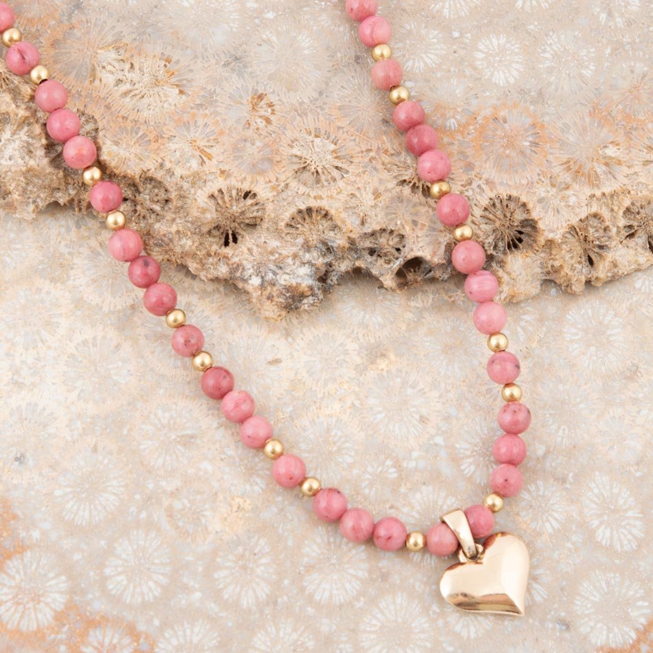 Necklace with pink beads and a gold heart pendant on a textured surface