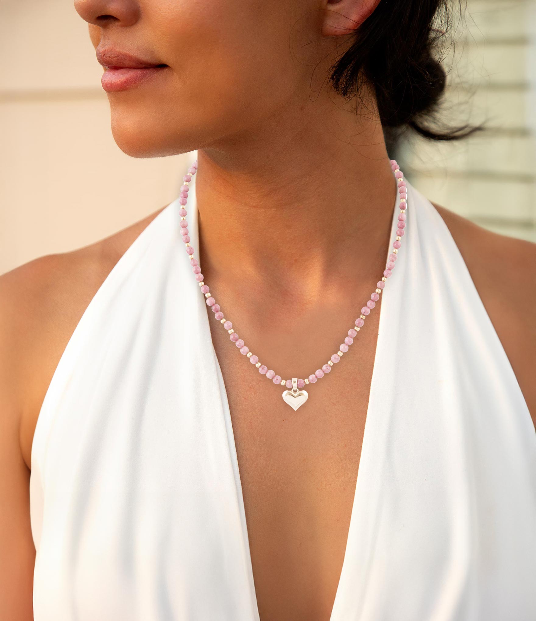 Close-up of a woman wearing a necklace with a heart pendant, dressed in a white top.