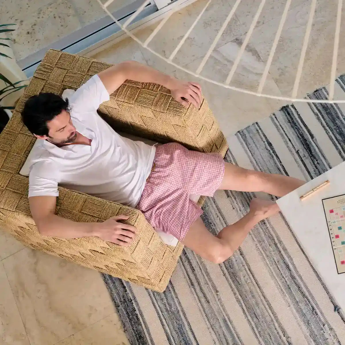 Man lying on a woven chair in a room with a striped rug and desk.