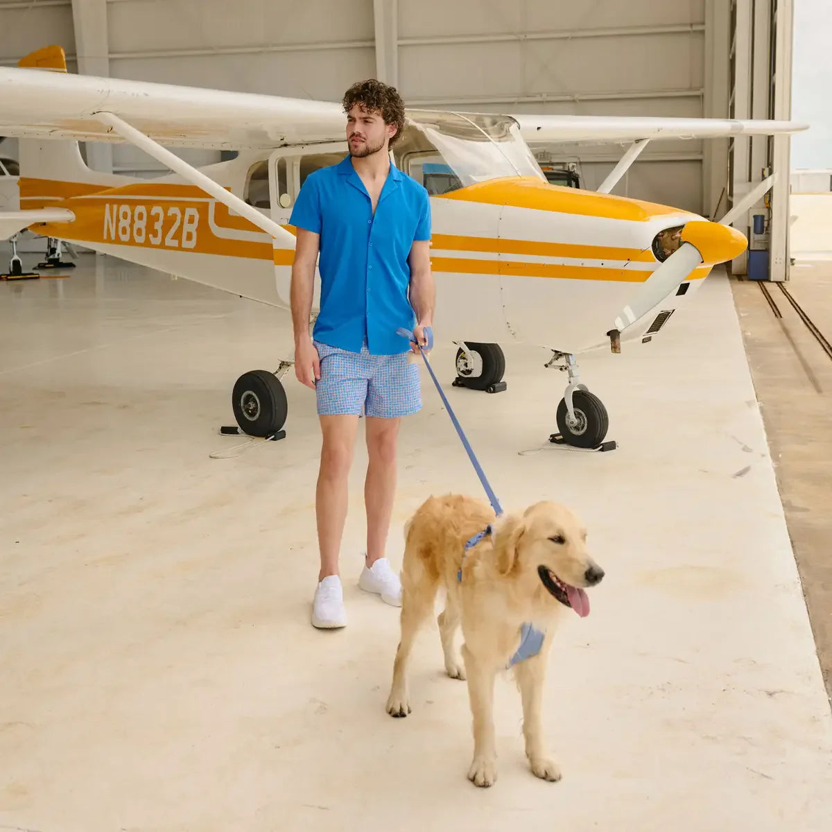 Man walking a dog in front of a small airplane inside a hangar
