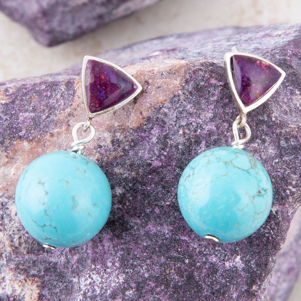 Pair of earrings with purple triangular stones and turquoise beads on a textured stone surface