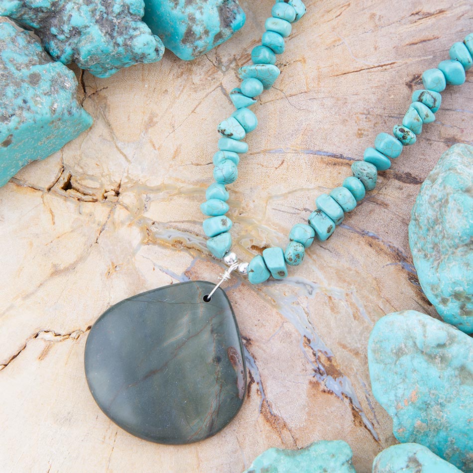 Turquoise beaded necklace with a large stone pendant on a textured beige surface.