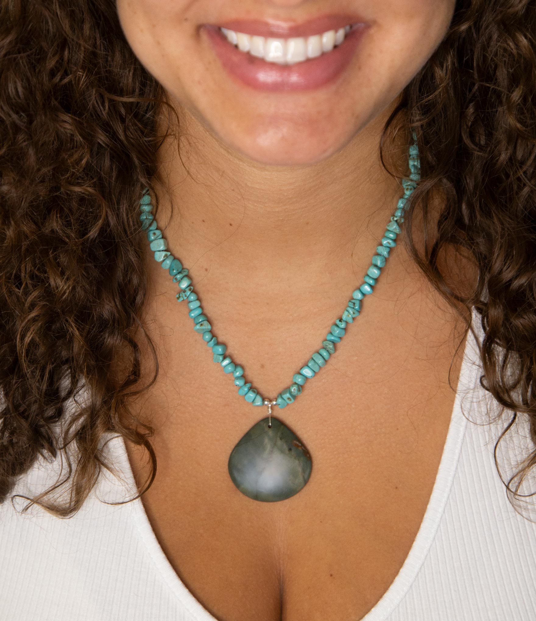 Woman wearing a turquoise beaded necklace with a large pendant.