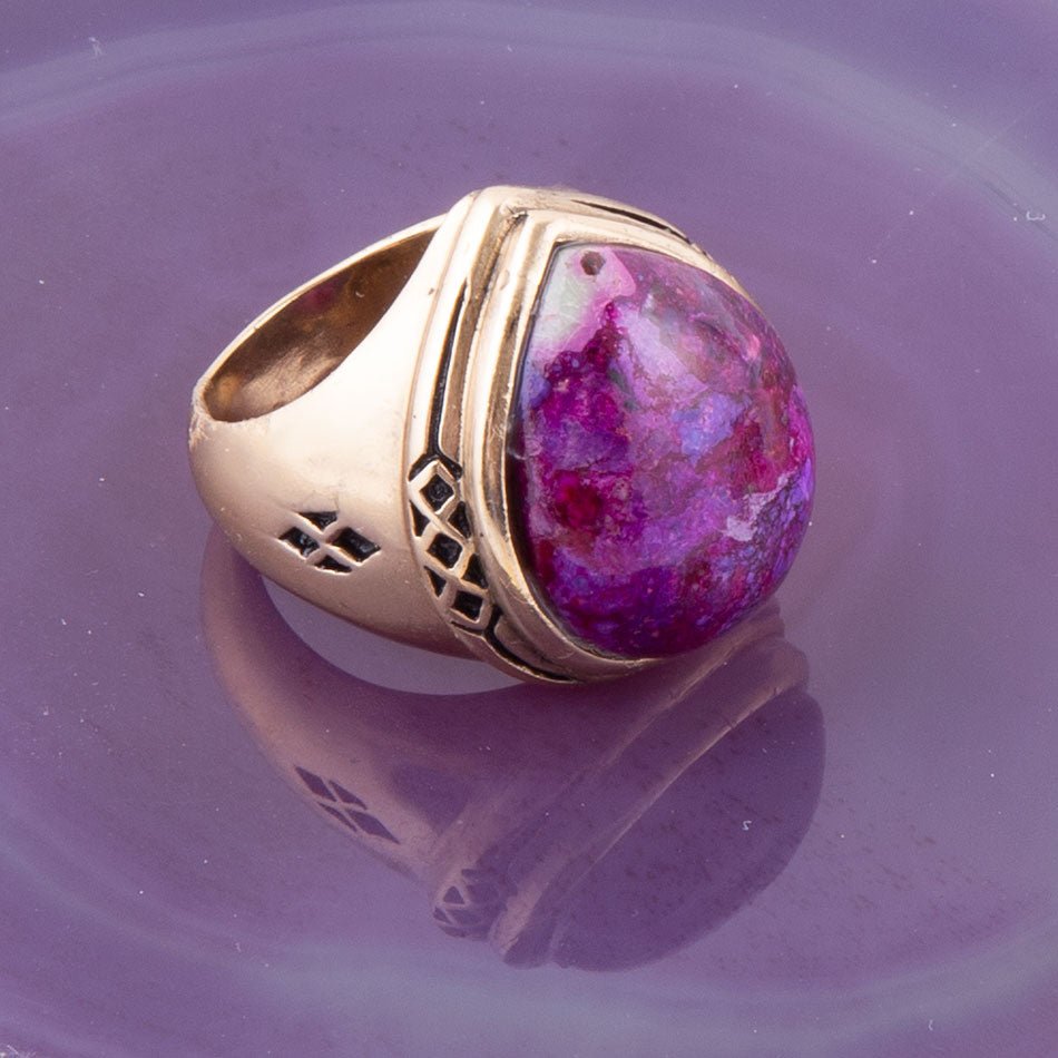 Gold ring with a purple gemstone on a reflective purple surface