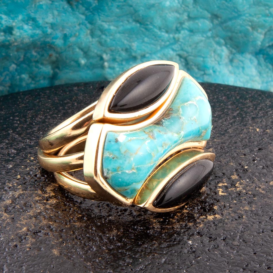 Gold ring with turquoise and black stone on a textured surface