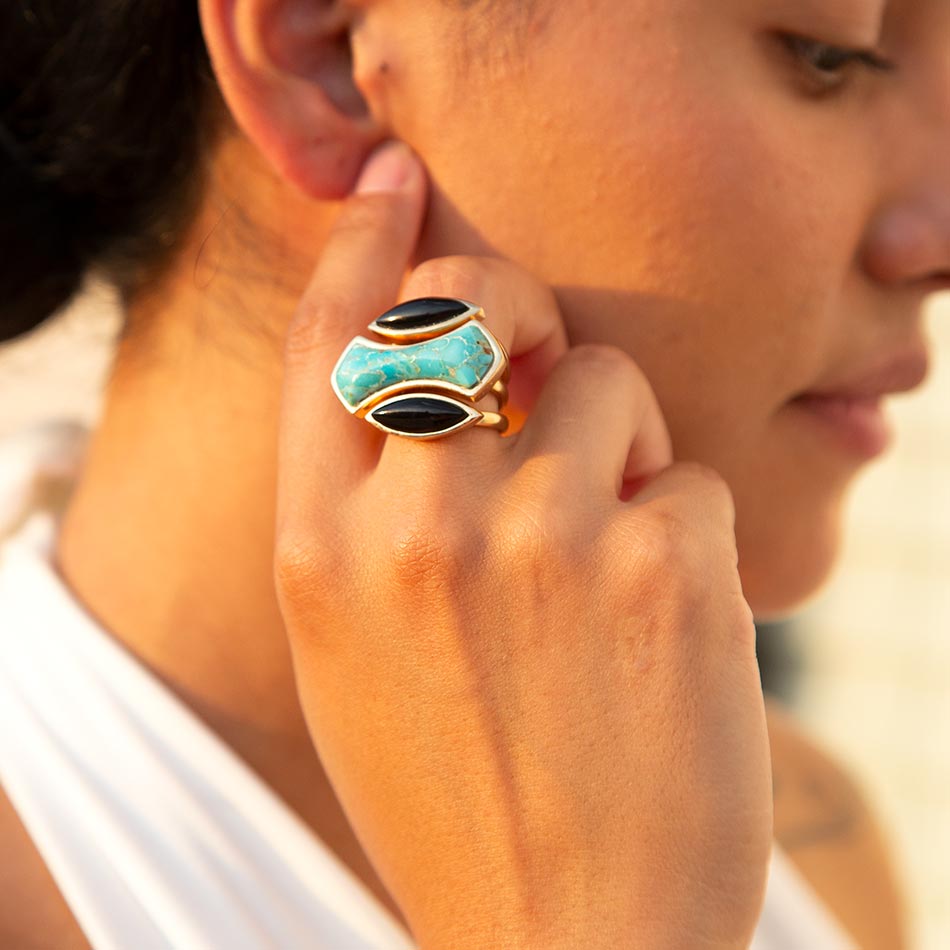 Close-up of a person wearing a turquoise and black ring on a blurred background