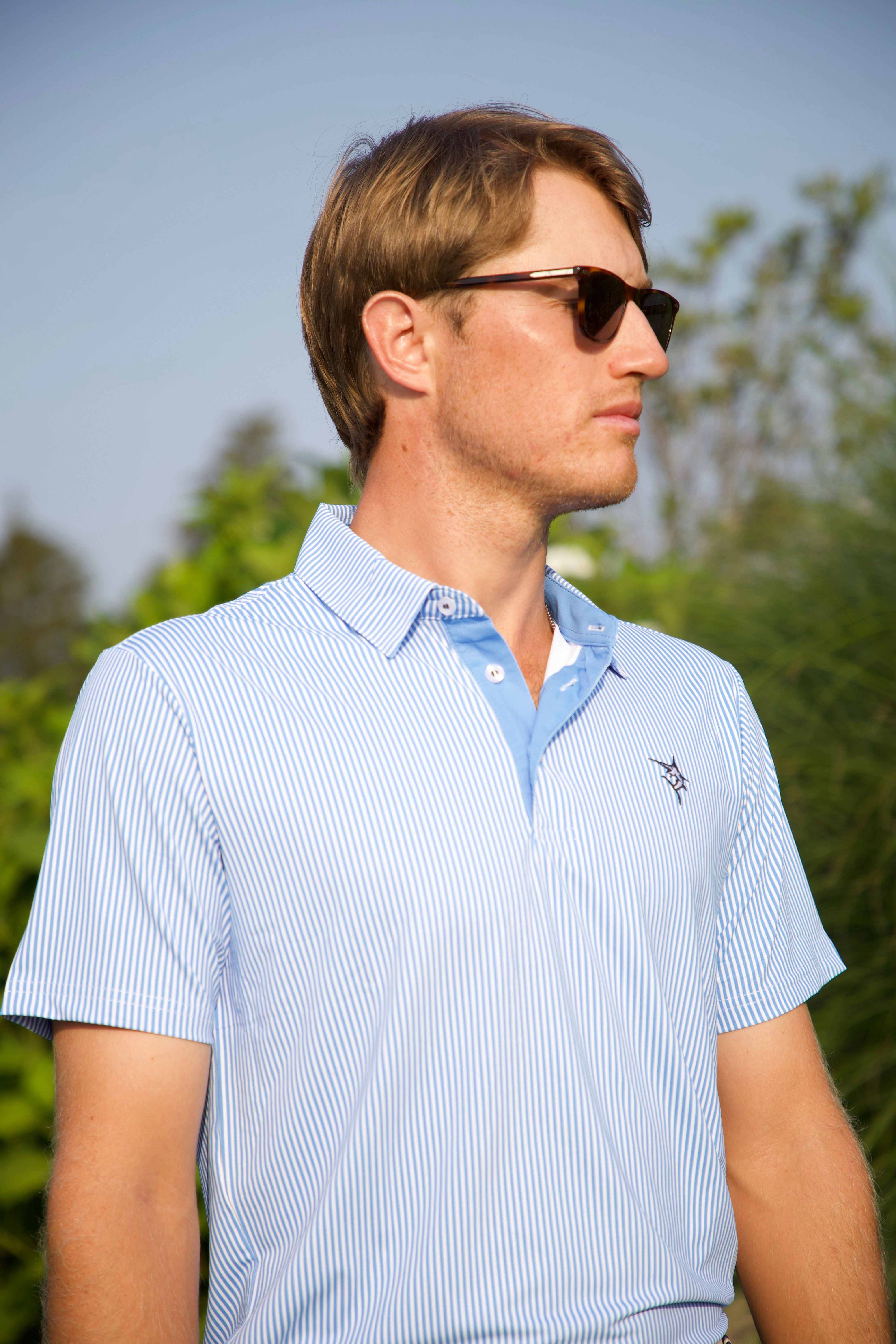 Man wearing a light blue striped polo shirt with a logo outdoors