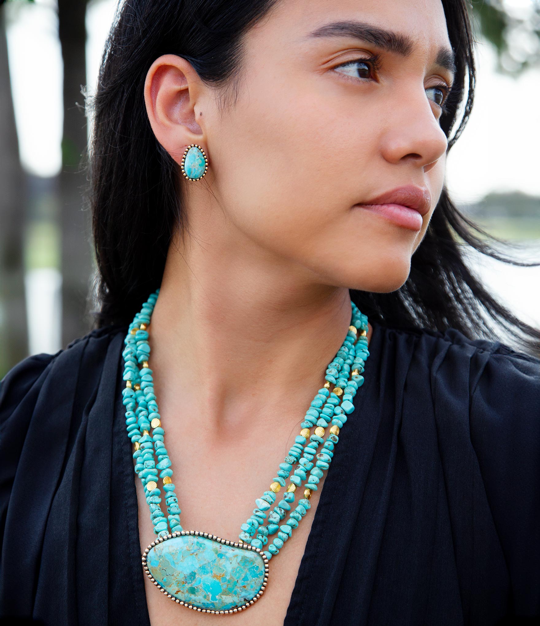 Woman wearing a turquoise necklace and earring with a blurred natural background