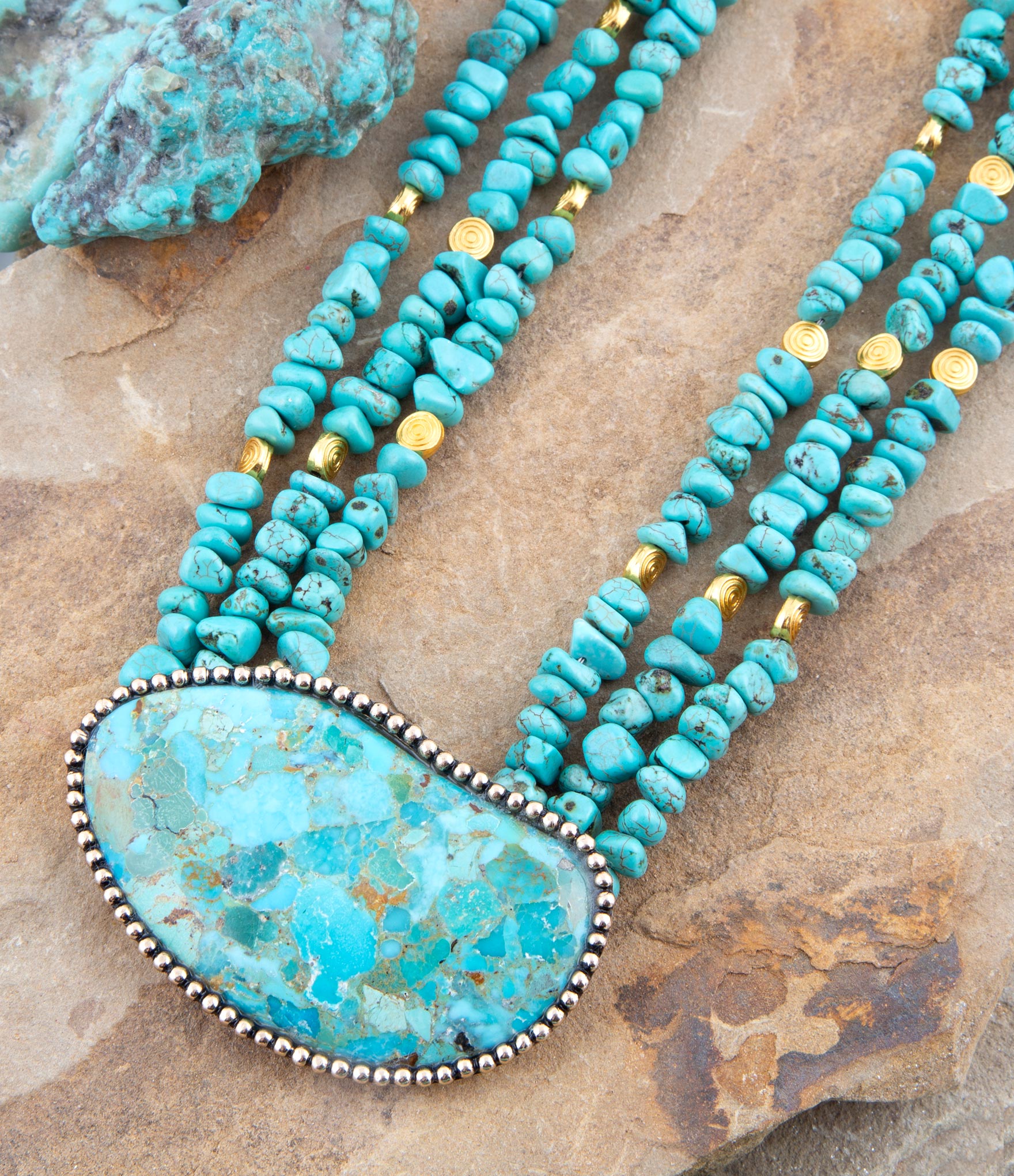 Turquoise beaded necklace with a large turquoise stone pendant on a stone surface