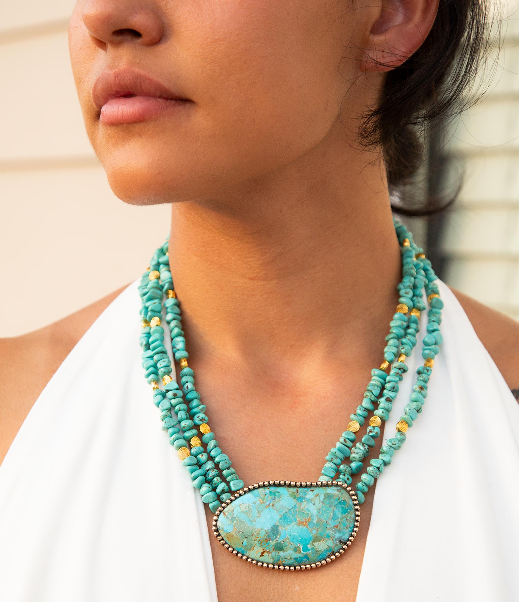 Turquoise beaded necklace with a large pendant worn by a person.