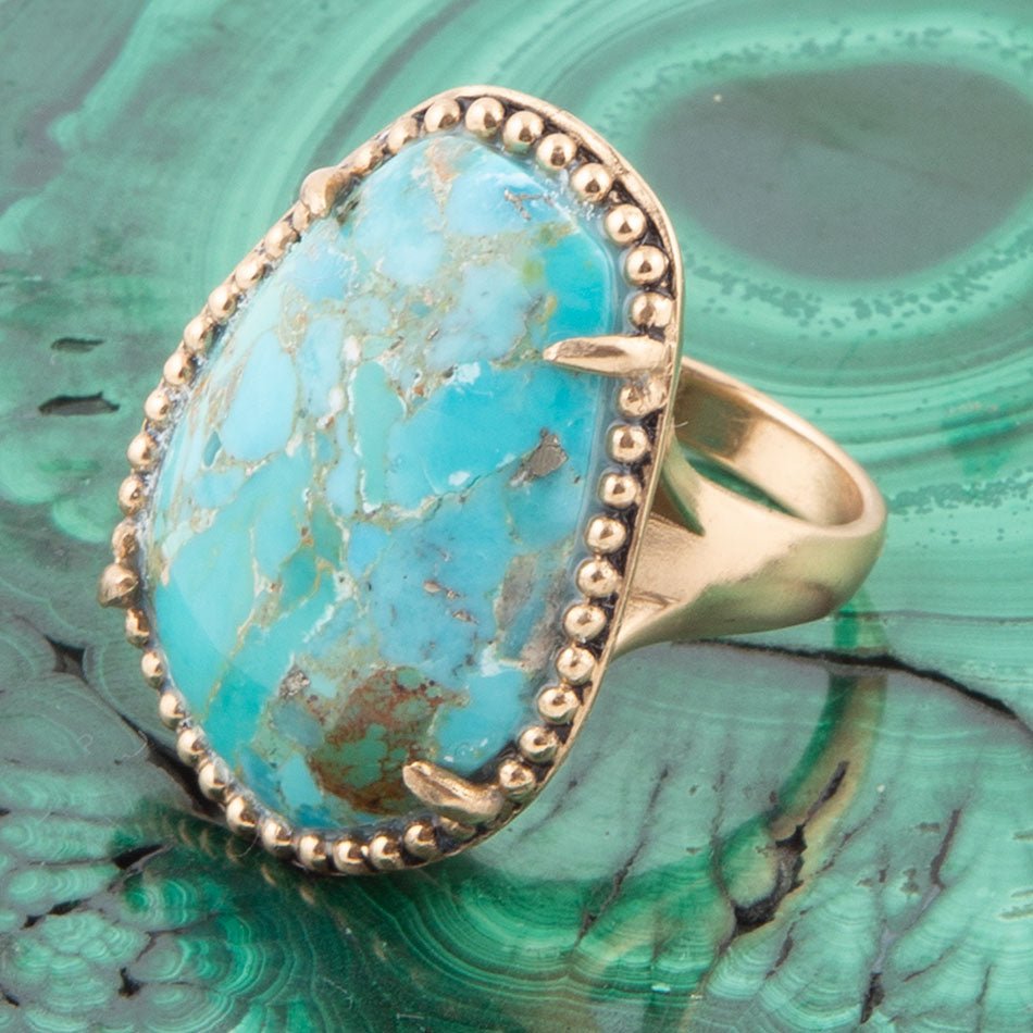 Gold ring with a large turquoise stone on a green marbled background