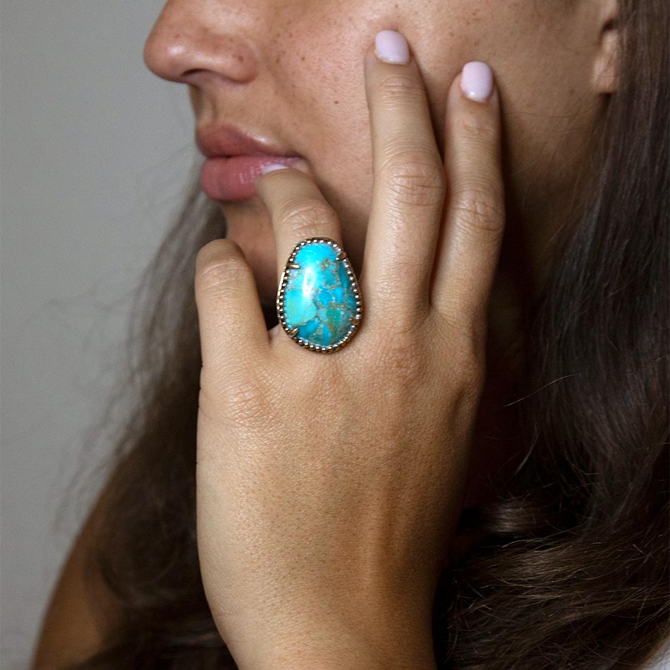 Close-up of a hand wearing a turquoise ring with a neutral background