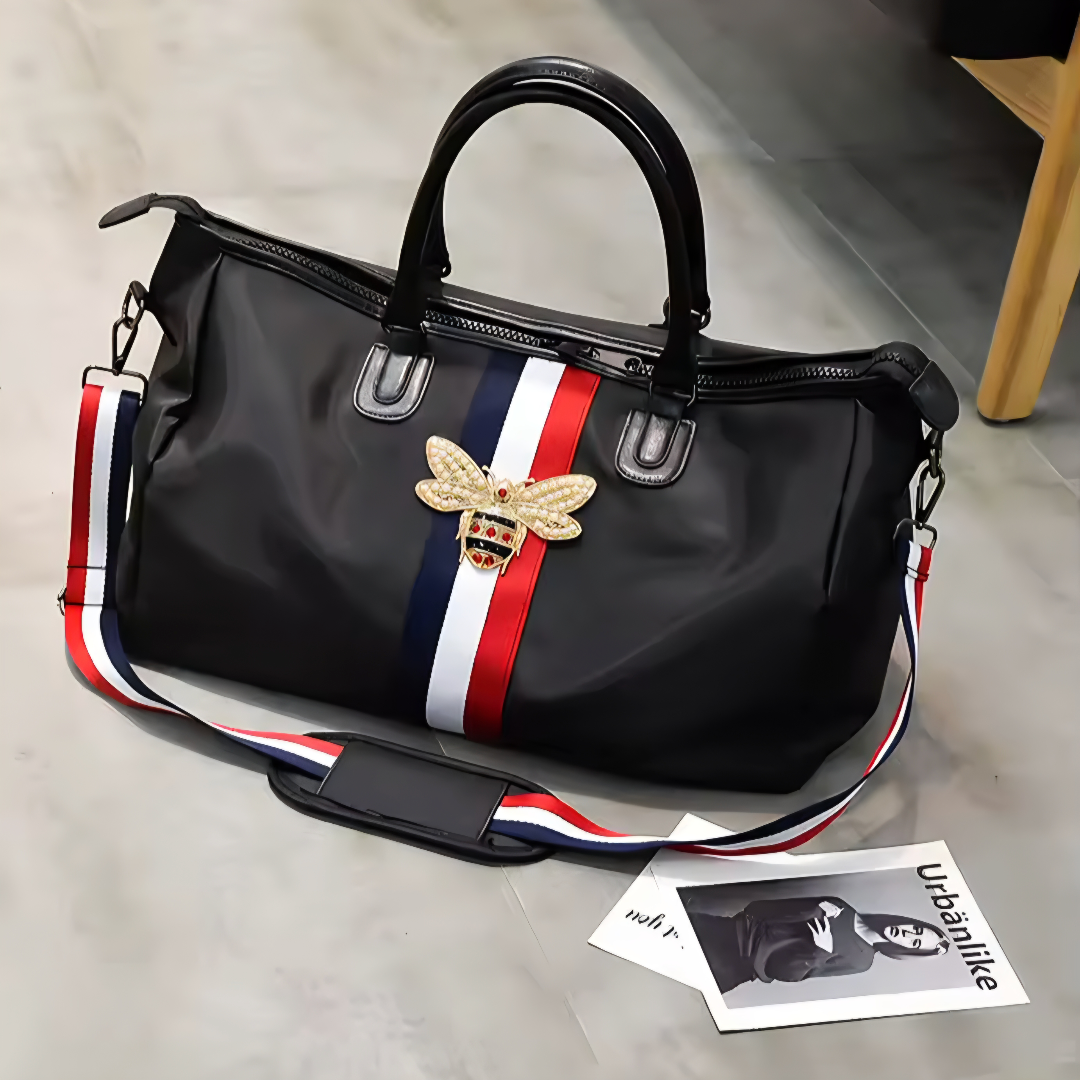 Black handbag with a bee emblem and colorful strap on a light surface
