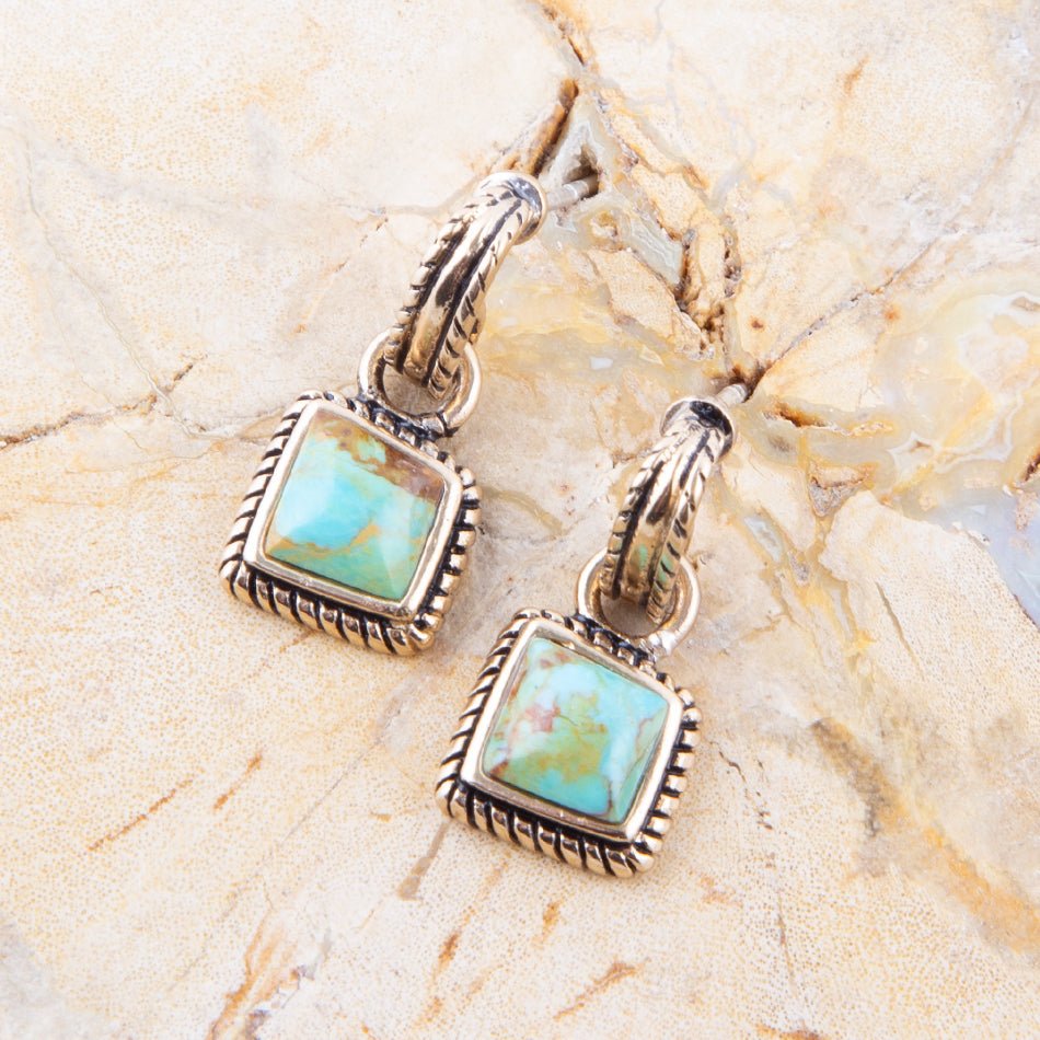 Pair of earrings with turquoise stones on a beige stone background