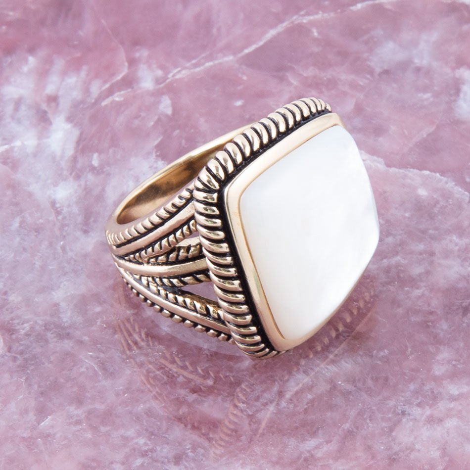 Gold ring with a white stone on a pink marble background