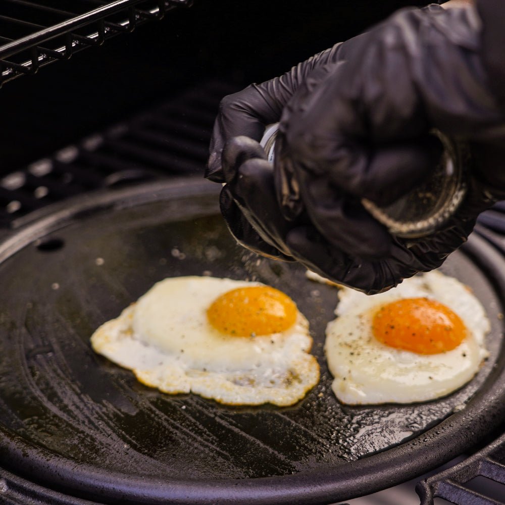 Person cooking eggs on a grill with a gloved hand
