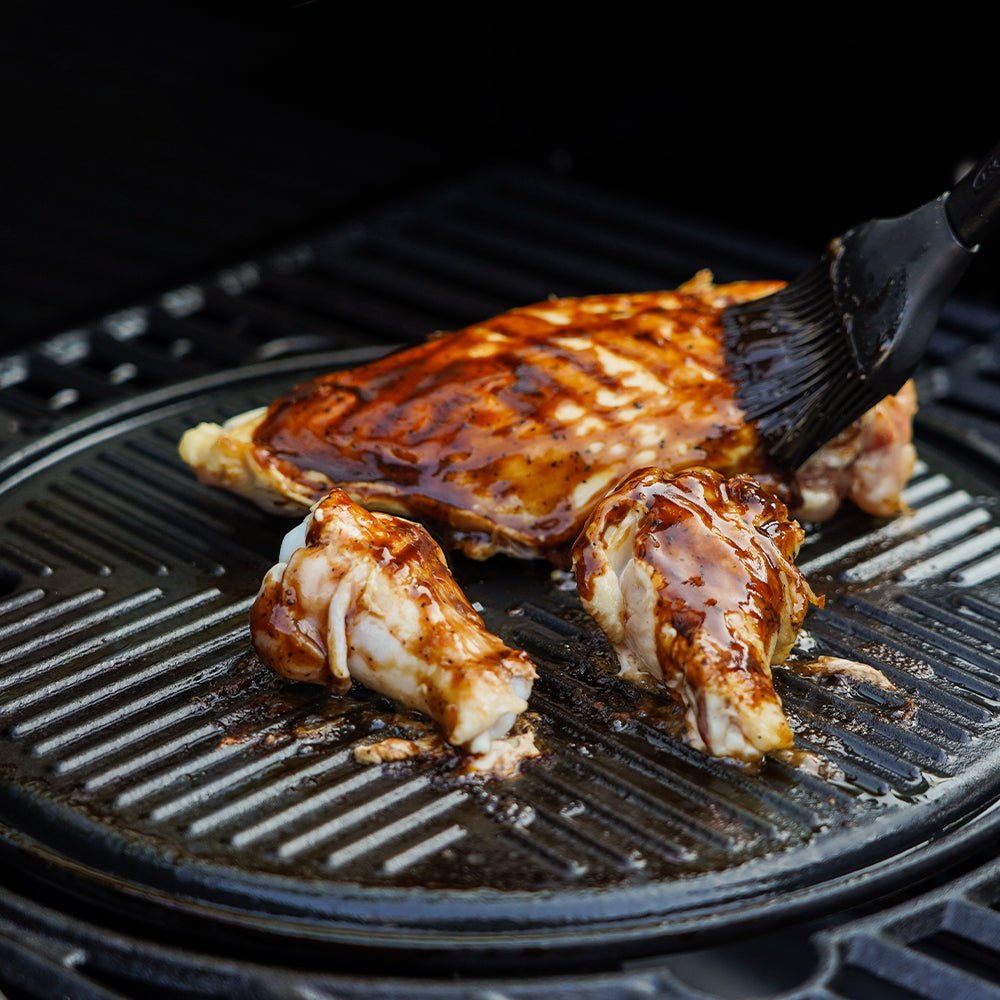 Chicken being grilled on a barbecue with a brush applying sauce.