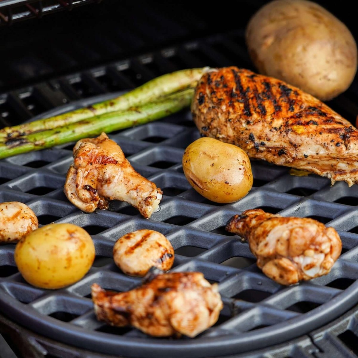 Grilled chicken pieces and vegetables on a grill grate